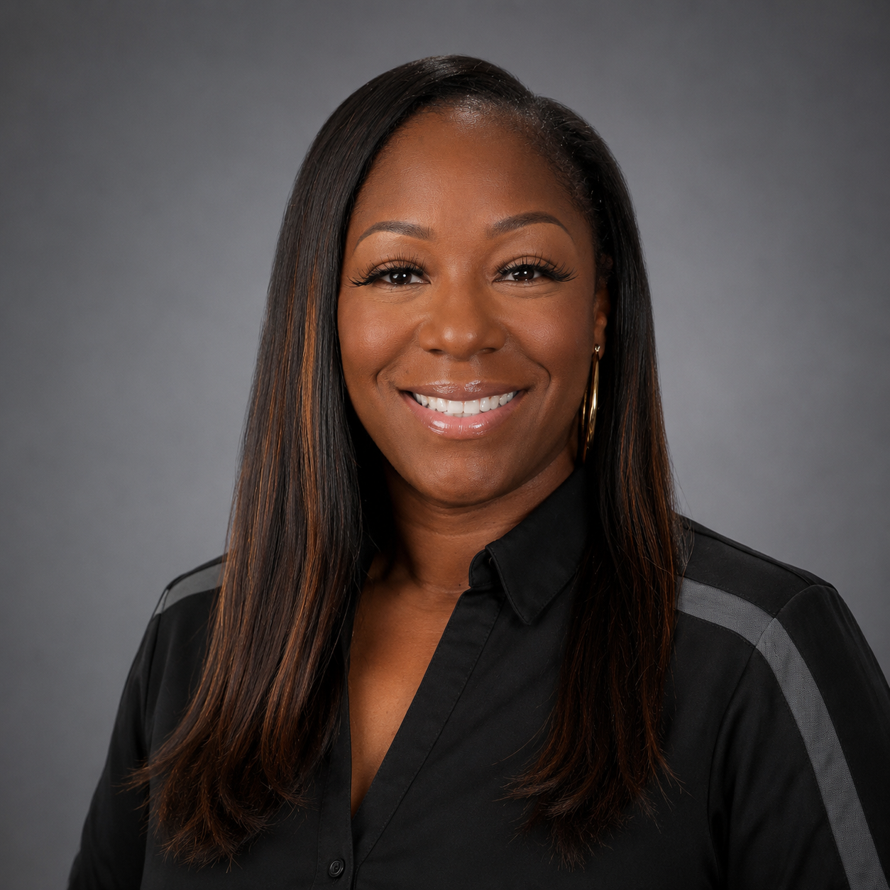 A woman with dark long hair wearing a black collard shirt and grey strip is smiling.